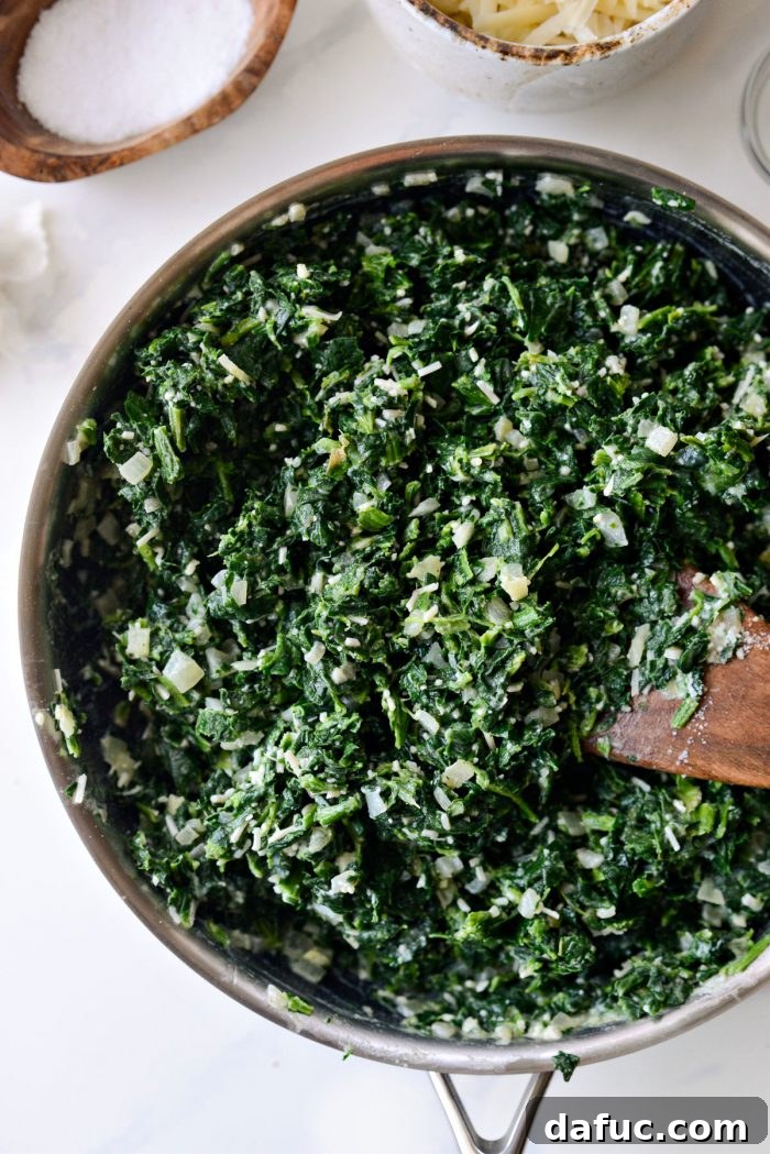 The spinach, cream, and Parmesan cheese mixture being thoroughly stirred in the skillet to combine all ingredients evenly.
