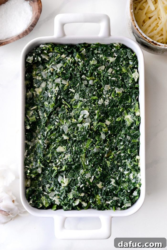 The creamy spinach mixture being transferred from the skillet into a lightly greased casserole dish, ready for baking.