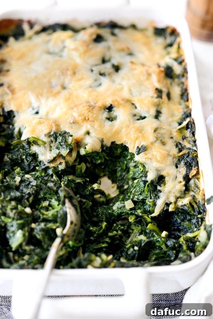 A full casserole dish of Spinach Gratin with a serving spoon, ready to be enjoyed at a festive meal.