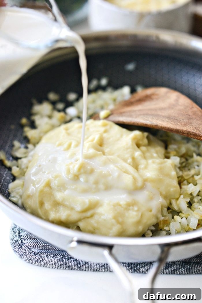The creamy condensed soup and whole milk being poured into the skillet with the sautéed aromatics, forming the rich gratin base.