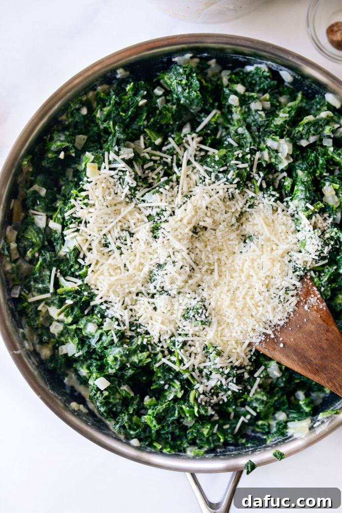 Grated Parmesan cheese being sprinkled over the spinach and cream mixture in the skillet.