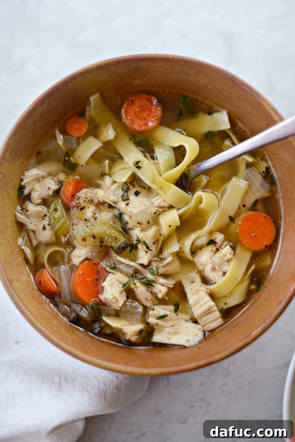 A steaming, inviting bowl of Leftover Turkey Noodle Soup, brimming with tender turkey pieces, vibrant vegetables, and comforting egg noodles in a clear, savory broth.