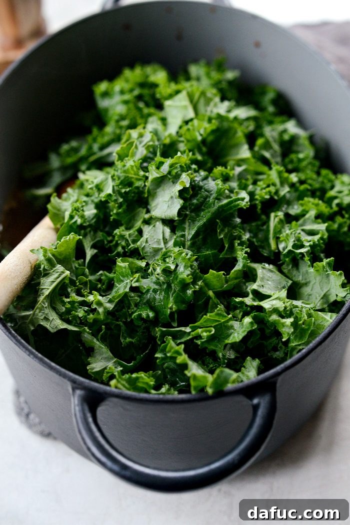 Chopped kale being added to the pot of Zuppa Toscana.