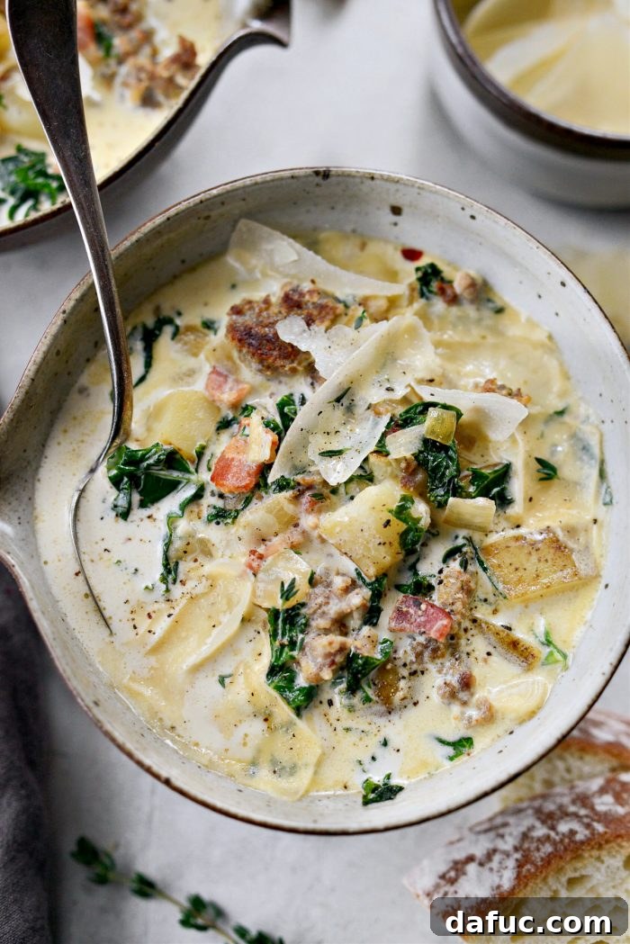 A beautifully composed shot of Zuppa Toscana in a bowl with a spoon, accompanied by fresh bread and herbs.