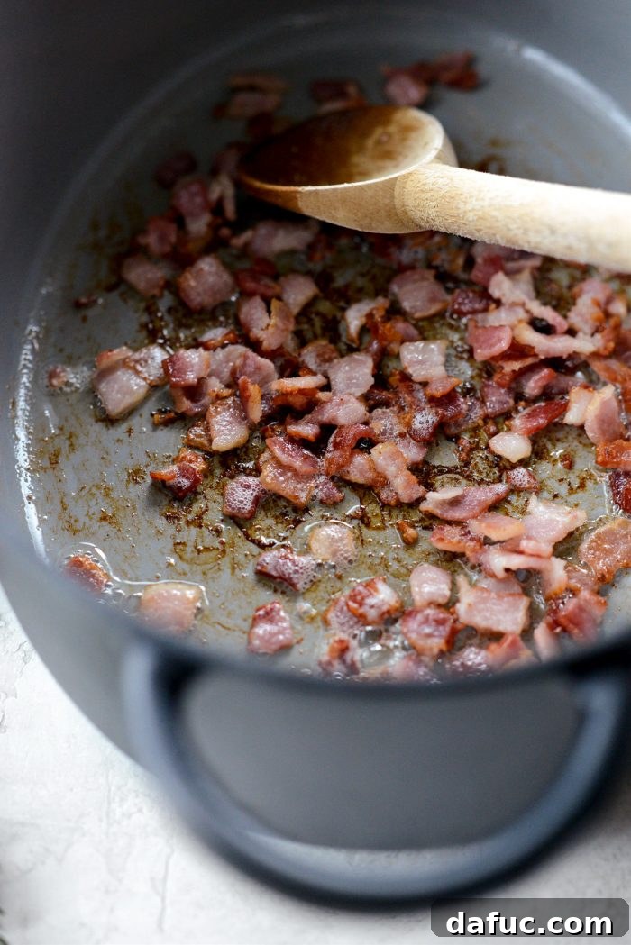 Diced center cut bacon sizzling and crisping in a Dutch oven.