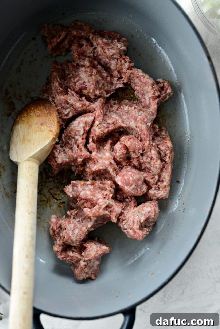 Uncooked ground hot Italian pork sausage added to the Dutch oven with reserved bacon fat.
