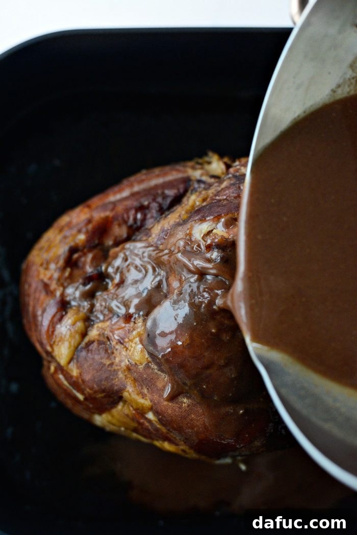 Jeweled Pomegranate Bourbon Glazed Ham 13 Hands pouring the thick Pomegranate Bourbon Glaze generously over the pre-baked spiral sliced ham in the roasting pan.