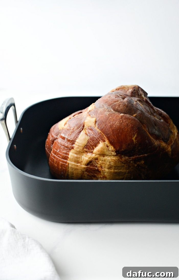Jeweled Pomegranate Bourbon Glazed Ham 5 A large, bone-in spiral sliced ham resting in a sturdy roasting pan, ready for its initial bake.