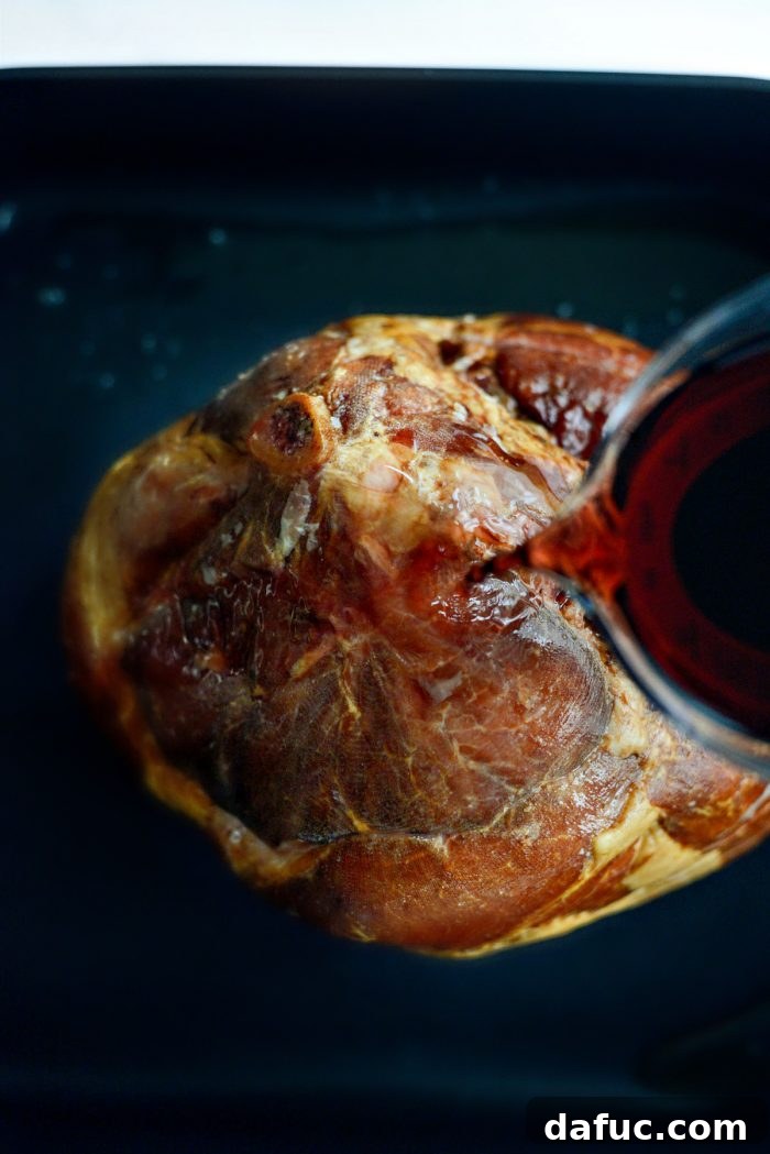 Jeweled Pomegranate Bourbon Glazed Ham 6 Hands pouring a mixture of pomegranate juice and bourbon over the spiral sliced ham in the roasting pan.
