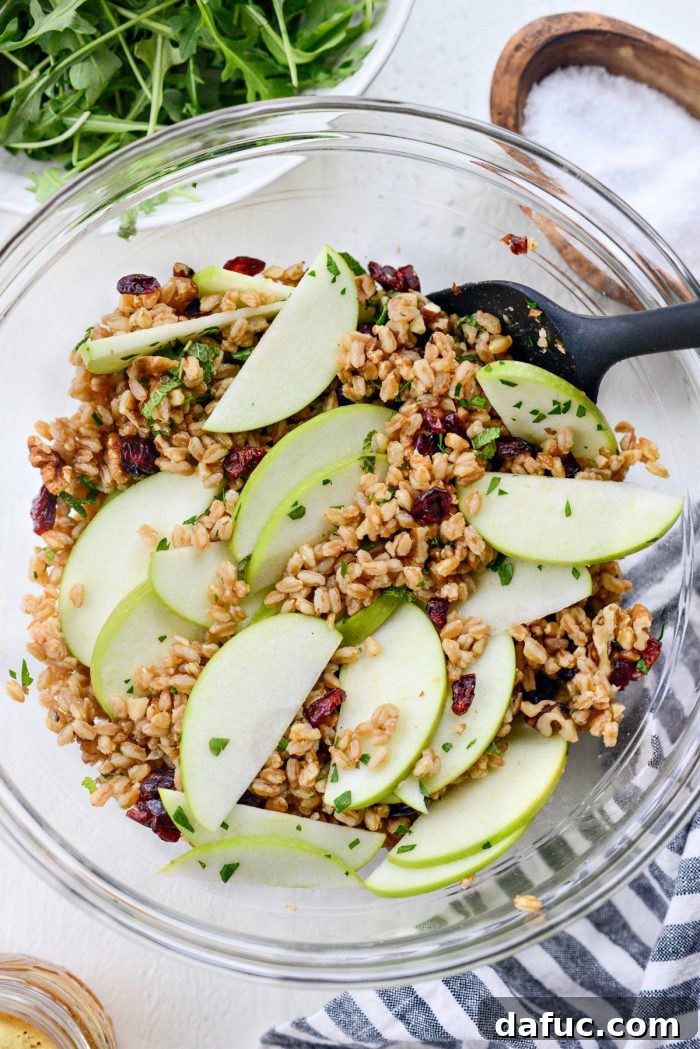 The process of gently tossing the ingredients of the winter farro salad in a bowl to ensure even mixing.