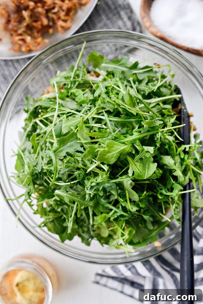 Fresh baby arugula being added to the bowl of mixed farro, fruits, nuts, and herbs for the winter salad.