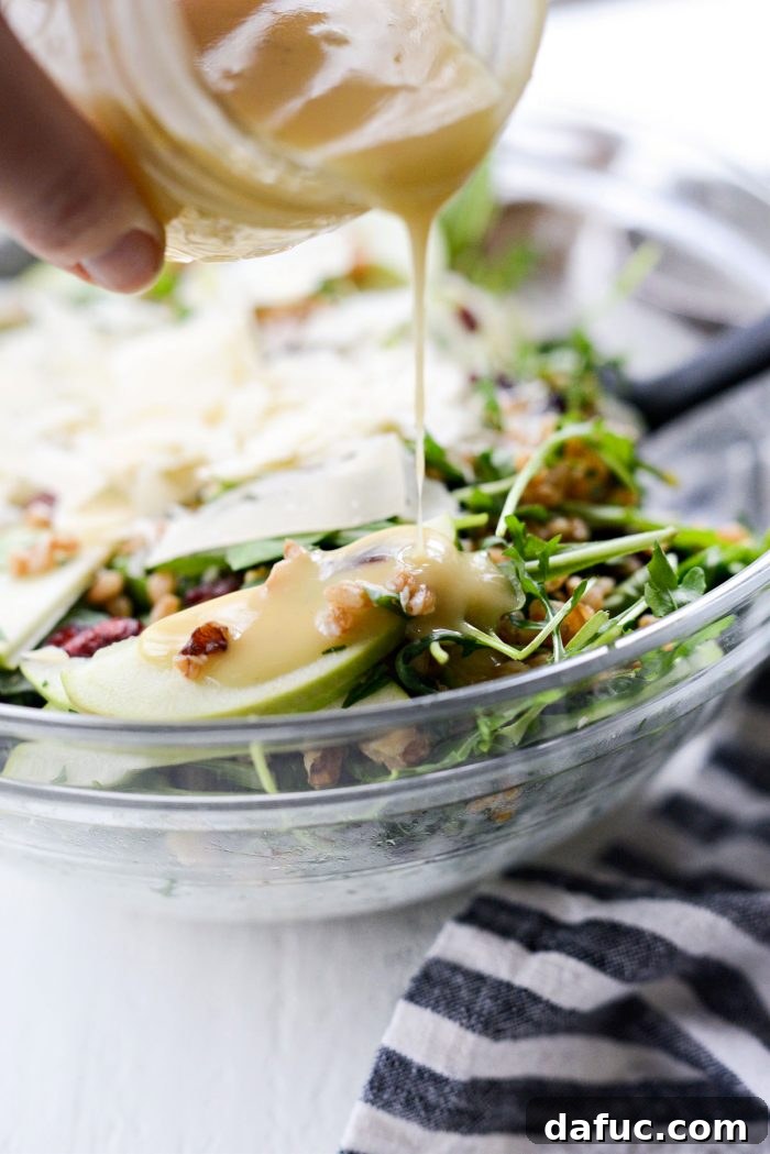 A generous amount of golden honey dijon dressing being poured over the winter farro salad in a large bowl.