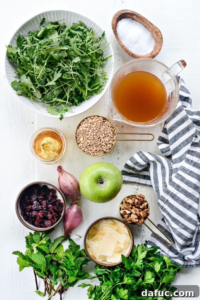 A selection of fresh ingredients for the Winter Farro Salad, including shallots, green apples, dried cranberries, and fresh herbs, artfully arranged on a cutting board.