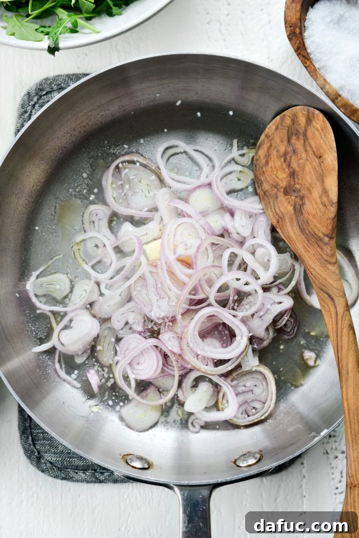 Thinly sliced shallots and butter sizzling in a skillet, beginning the process of becoming crispy fried shallots.