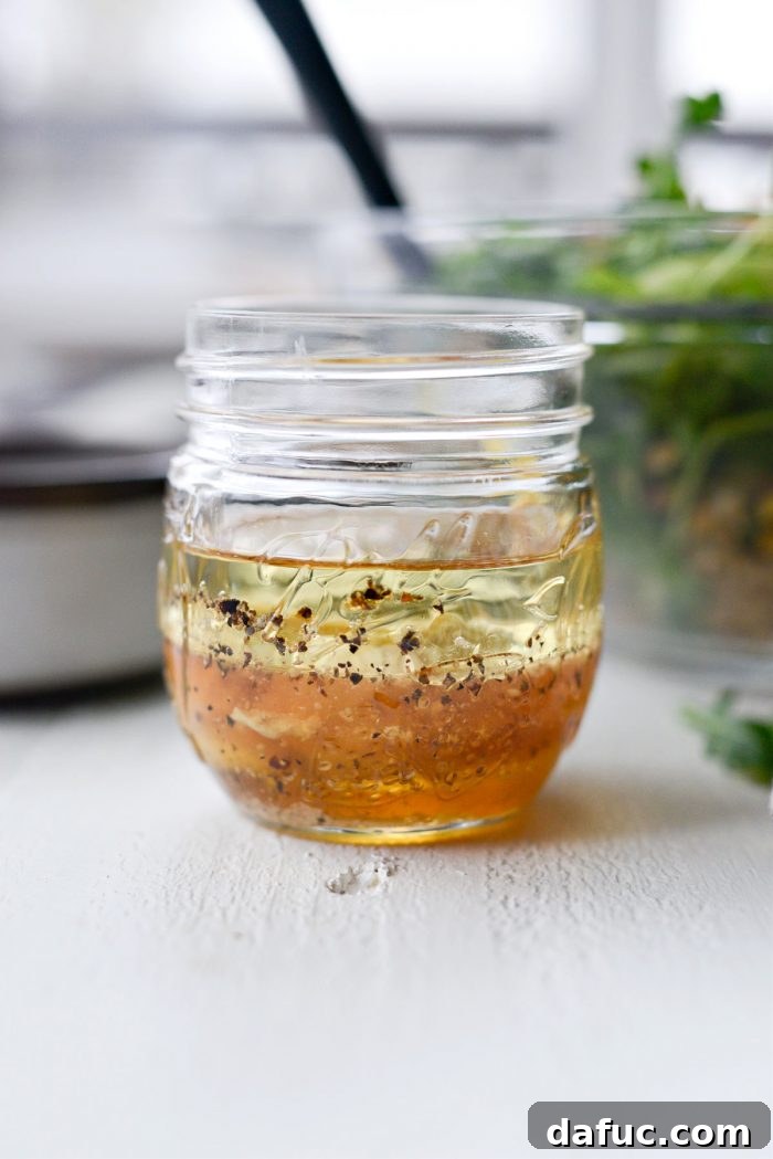 A vibrant honey dijon dressing being whisked in a glass jar, showing its creamy texture and golden hue.