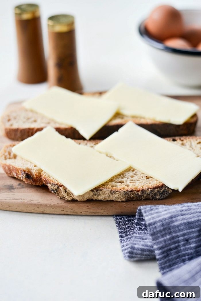 A slice of toasted sourdough bread topped with a slice of white American cheese, beginning to soften from the residual heat, ready for the fried eggs.