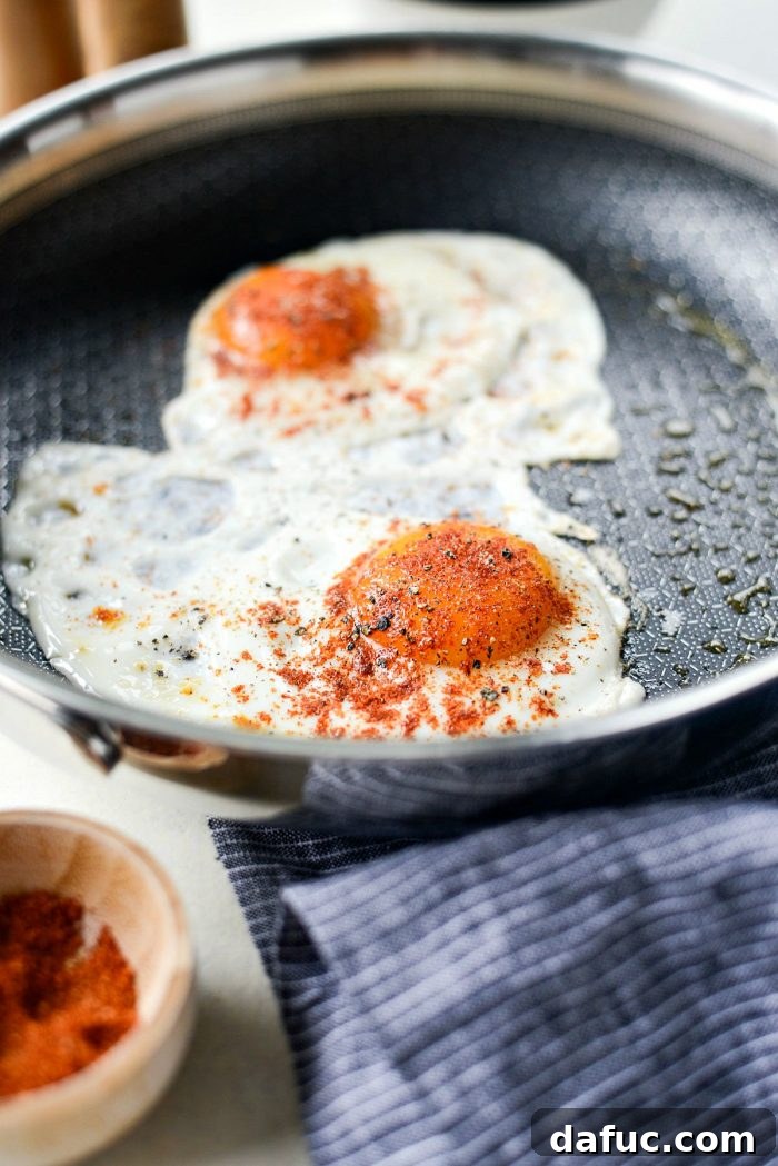 Fried eggs, perfectly seasoned with all-purpose salt and black pepper, cooking in a skillet, with whites set and yolks just beginning to firm, ready to be flipped.
