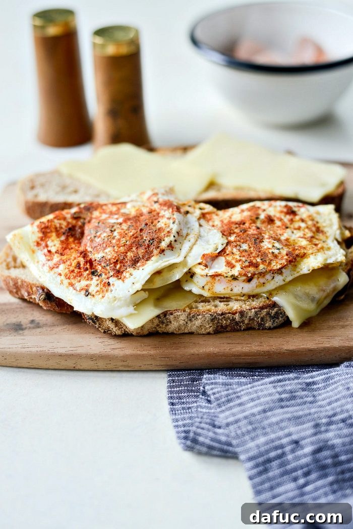 Two fried eggs with perfectly set whites and runny yolks, ready to be lifted from the skillet and placed onto toasted bread with melted cheese.