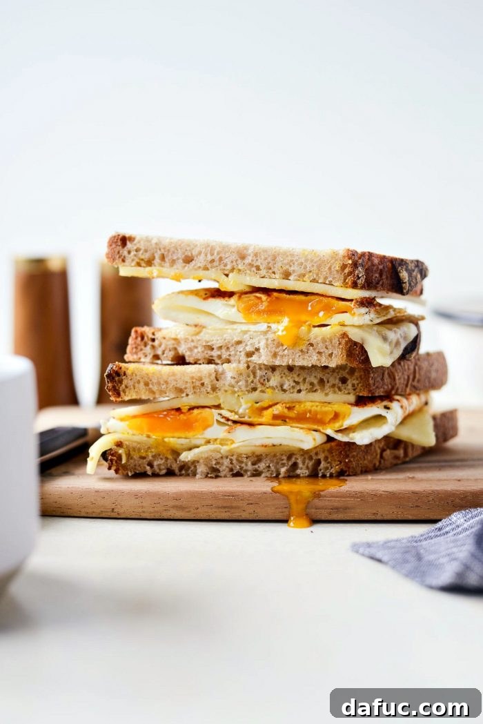 A perfectly cut fried egg sandwich, showing the beautiful layers of egg, melted cheese, and toasted bread, ready for enjoyment.