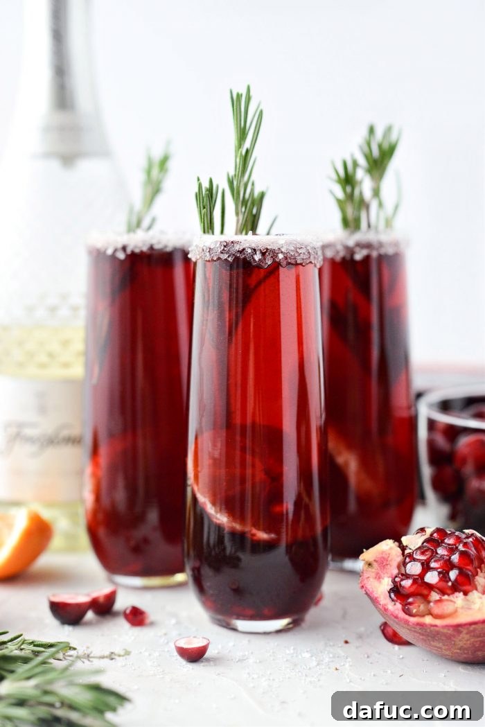 Bright & Bubbly Christmas Mornings 2 Christmas Morning Mimosas in sugar-rimmed glasses, garnished with cranberry, clementine, and rosemary