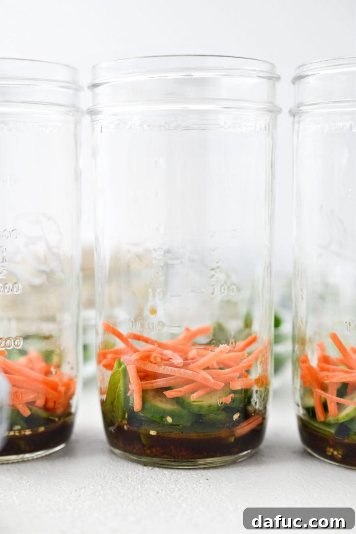 Mason jar with dressing, sugar snap peas, cucumber, and julienned carrots layered at the bottom.