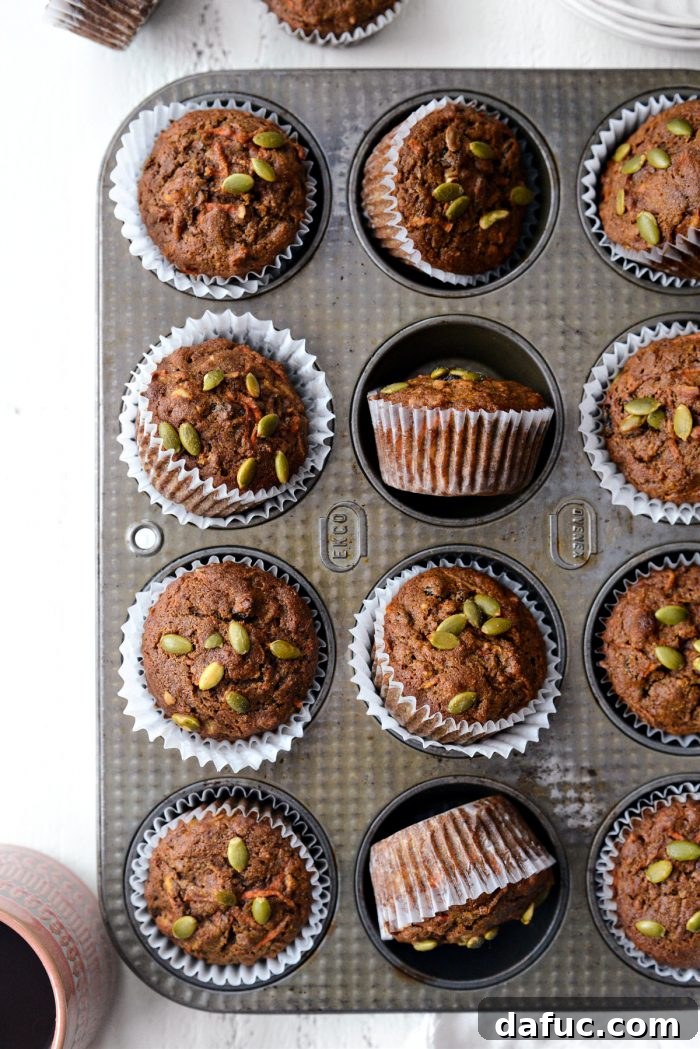 Batch of freshly baked Morning Glory Muffins in a muffin tin, golden brown and topped with pepitas.