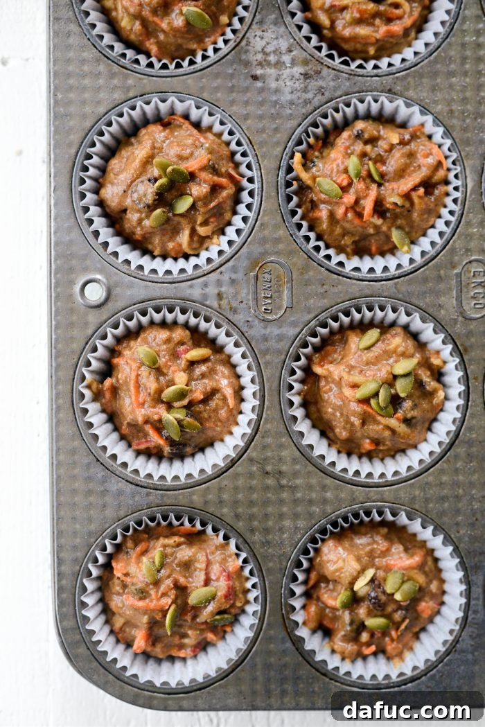 Muffin liners filled with Morning Glory batter, topped with pepitas, ready for baking.