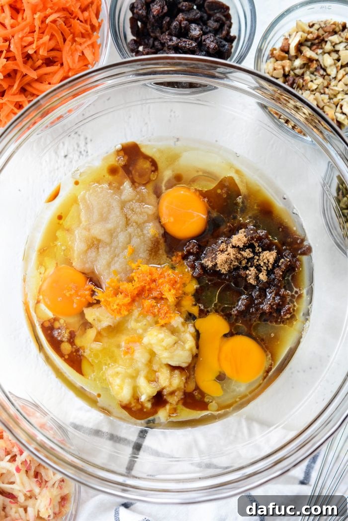 Wet ingredients in a large mixing bowl: eggs, brown sugar, maple syrup, mashed banana, applesauce, oil, vanilla, orange zest and juice.