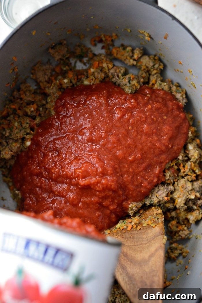 Slow Roasted Spaghetti Sauce 12 Crushed tomatoes and tomato sauce being poured into the Dutch oven with the meat and vegetable mixture.