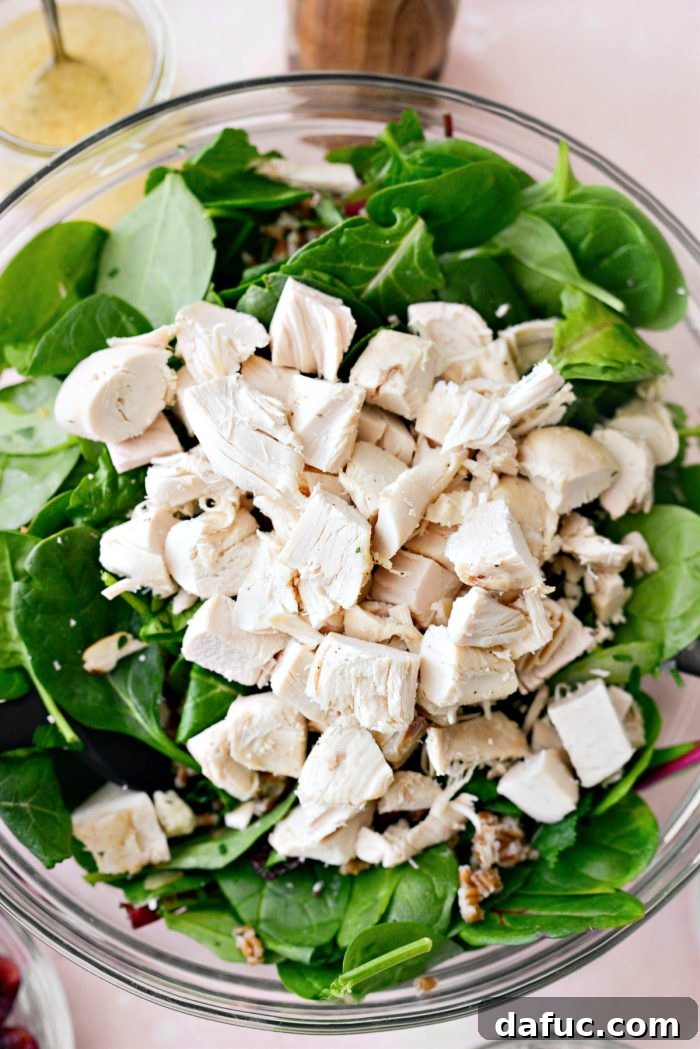 Adding chopped cooked chicken breast to the salad ingredients in the bowl