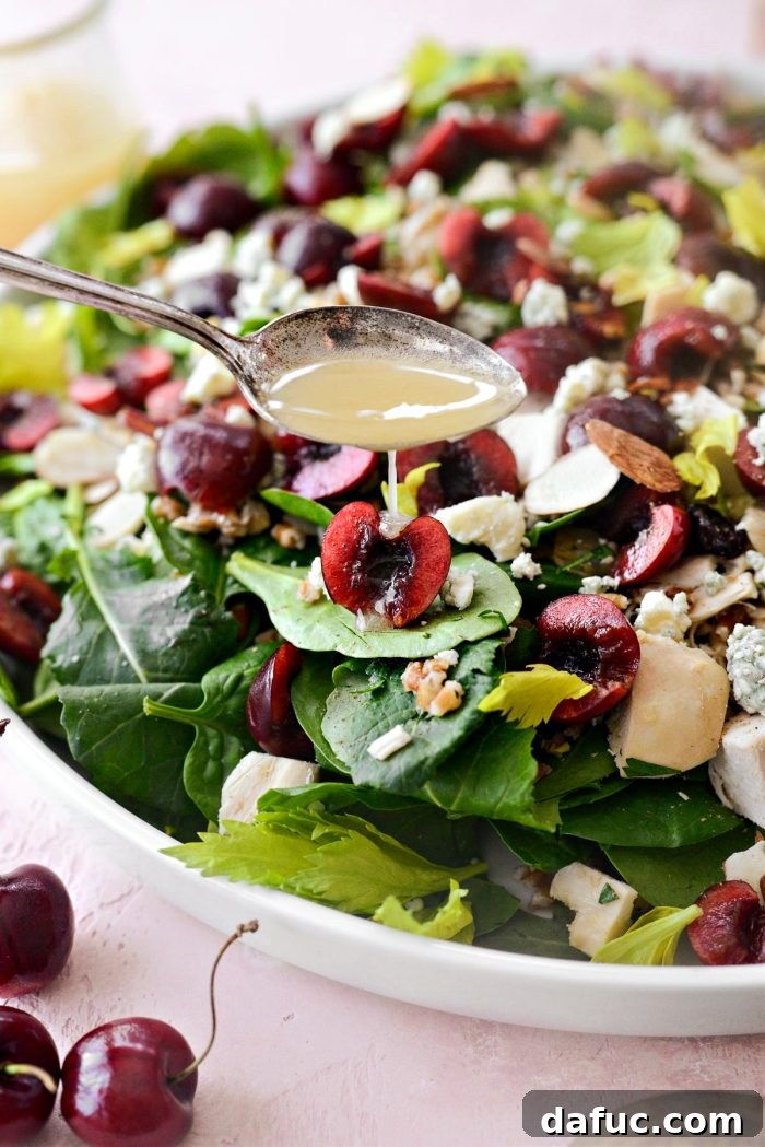 Drizzling apple cider vinaigrette over the completed Cherry Winter Wheat Berry Salad on a platter