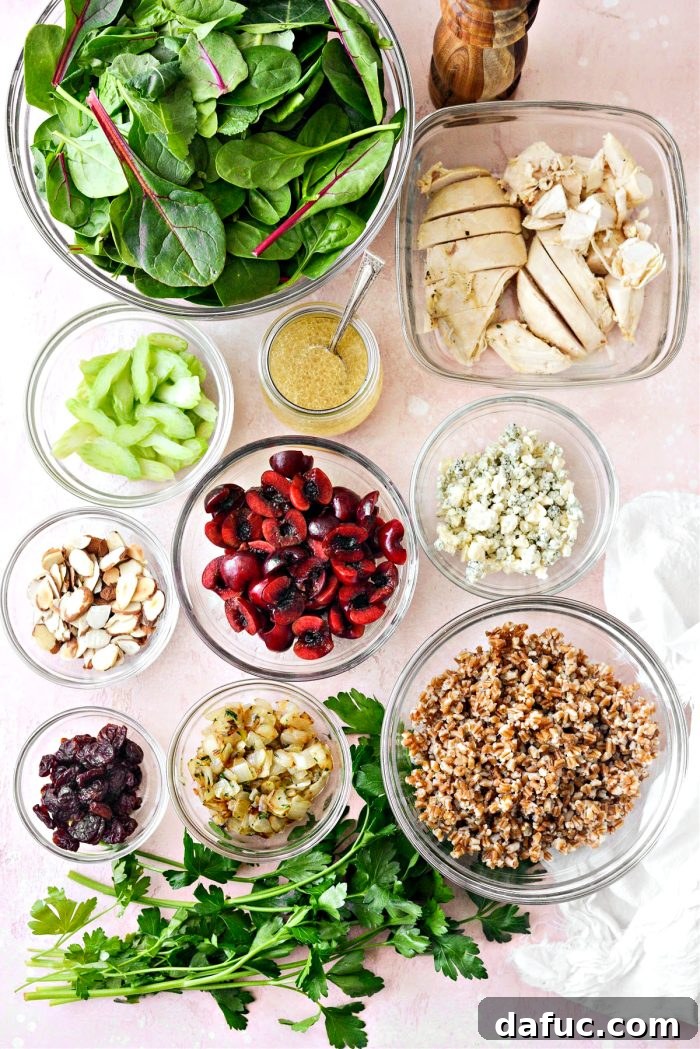 Ingredients laid out for Cherry Winter Wheat Berry Salad, including fresh cherries, dried cherries, wheat berries, blue cheese, almonds, celery, onion, thyme, chicken, and greens