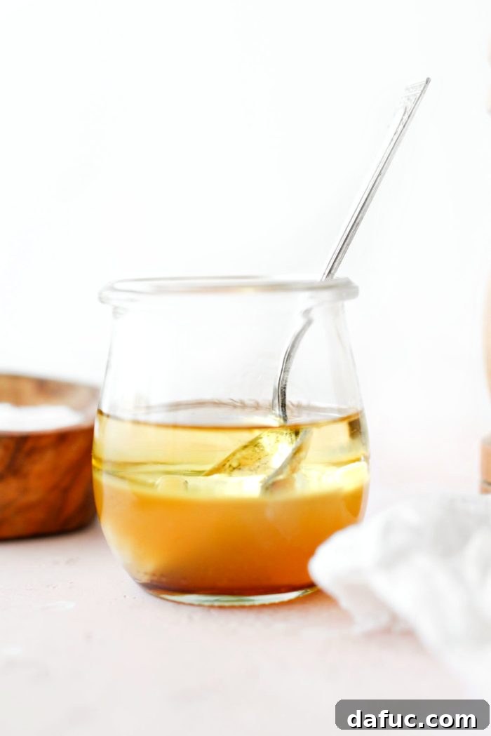 Ingredients for homemade apple cider vinaigrette in a glass jar, including apple cider vinegar, maple syrup, dijon mustard, garlic, and olive oil