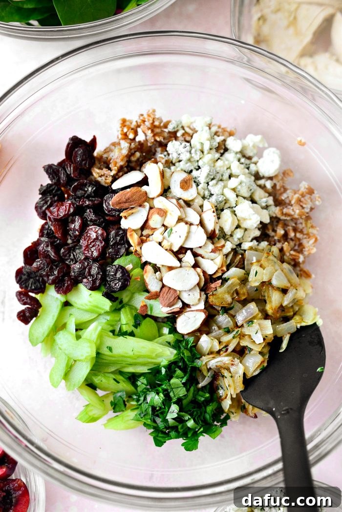 Adding various salad toppings like wheat berries, sautéed onions, almonds, celery, dried cherries, blue cheese, and parsley to a large mixing bowl