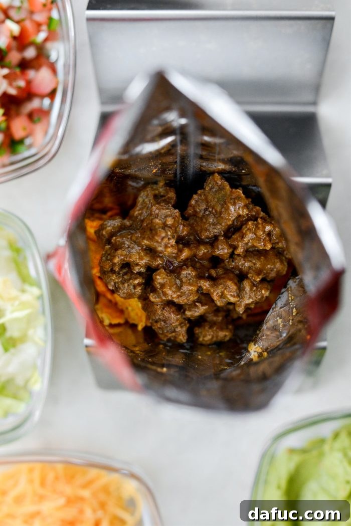 Walking Tacos Two Ways 11 Saucy taco meat being added to a bag of crushed Doritos.