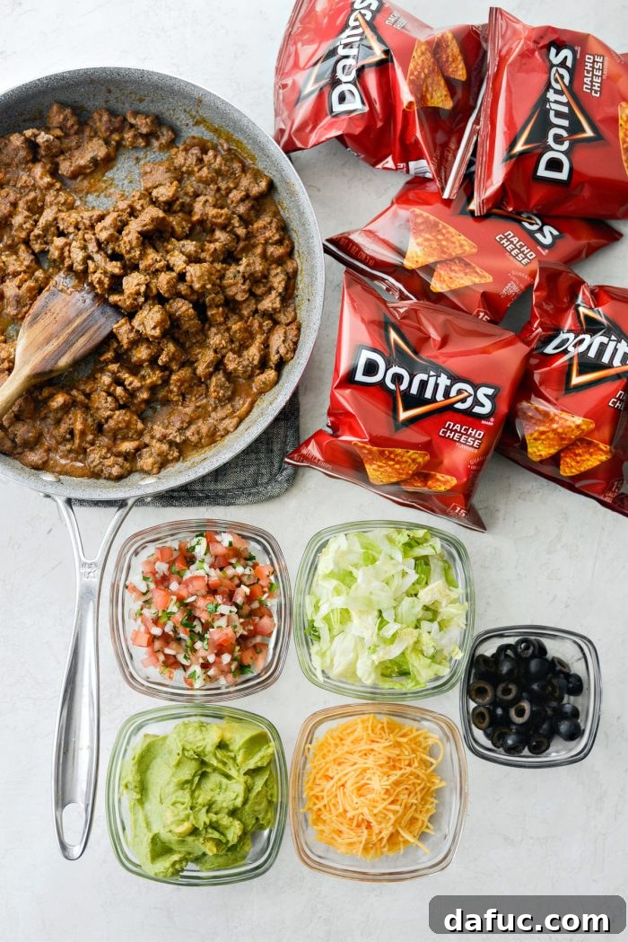 Walking Tacos Two Ways 3 Ingredients for beef taco walking tacos laid out including Doritos, lettuce, pico de gallo, guacamole, cheese, and black olives.