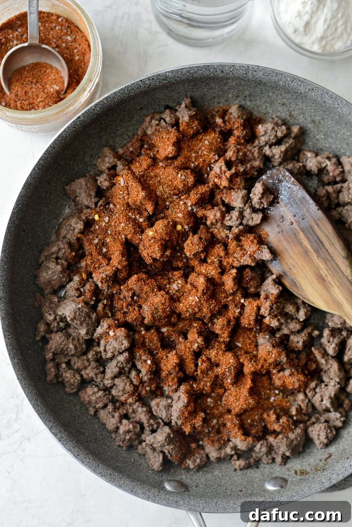 Walking Tacos Two Ways 5 Taco seasoning sprinkled over cooked ground beef in a skillet.