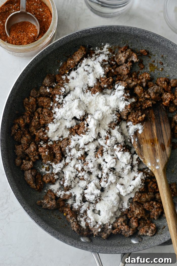 Walking Tacos Two Ways 6 Flour sprinkled over seasoned taco meat in a skillet.