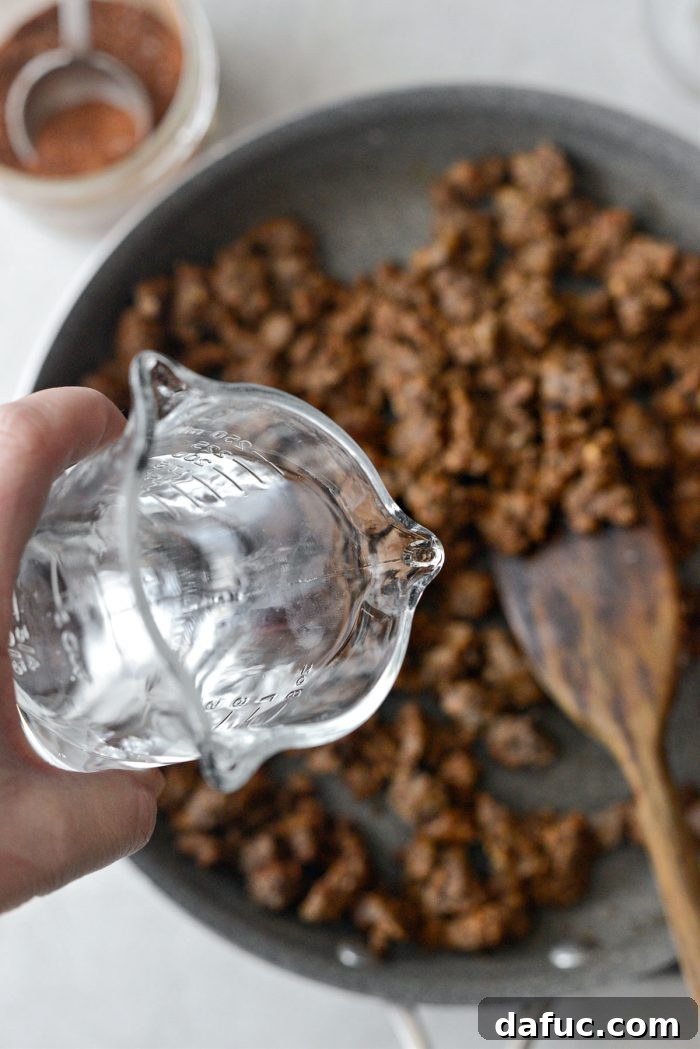 Walking Tacos Two Ways 8 Water being poured into the seasoned ground beef in a skillet.
