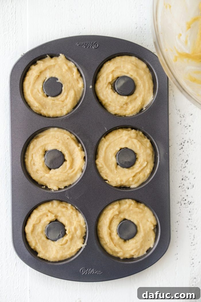 Doughnut pan cavities being filled with batter, approximately three-quarters full.
