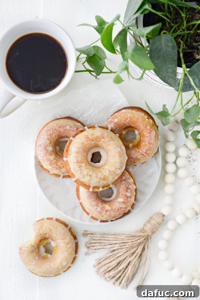 A stack of Glazed Buttermilk Cake Doughnuts artfully arranged next to a steaming cup of coffee, inviting indulgence.