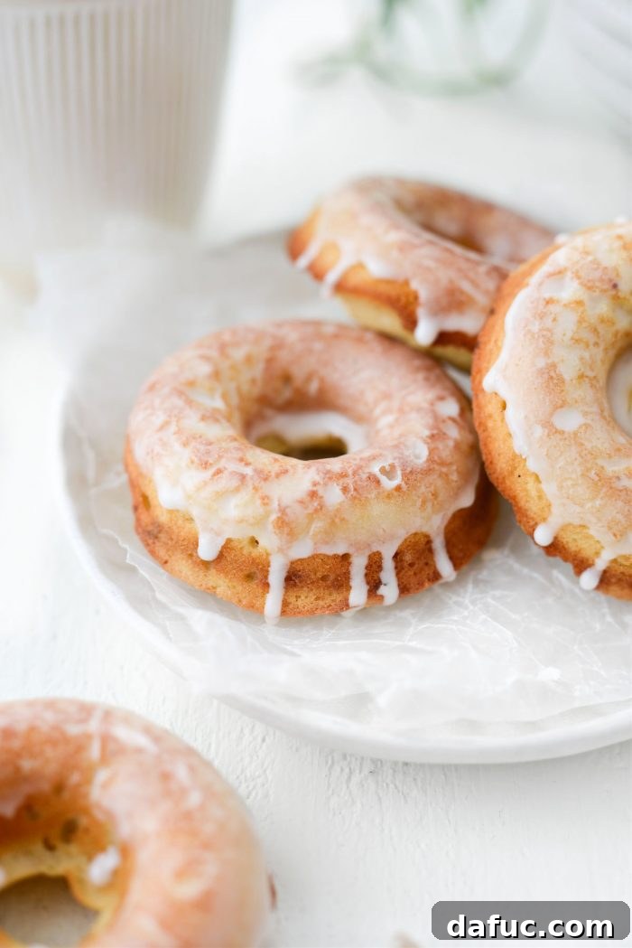 A close-up of a hand holding a Glazed Buttermilk Cake Doughnut next to a cup of coffee, emphasizing a perfect pairing.