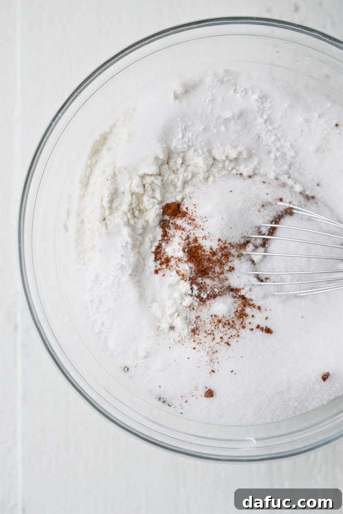 Dry ingredients for doughnuts (flour, sugar, baking powder, spices, salt) in a medium mixing bowl, ready to be whisked.