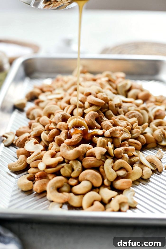 Decadent Honey Roasted Cashews 7 Pouring the honey-maple glaze over cashews on a baking sheet.