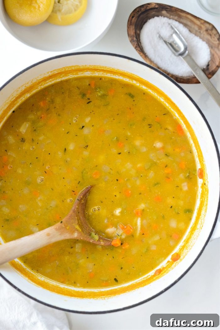 Sunshine Chickpea Bowl 15 A hand seasoning the bubbling lemon chickpea soup with kosher salt from a small bowl, enhancing its delicious flavor profile.