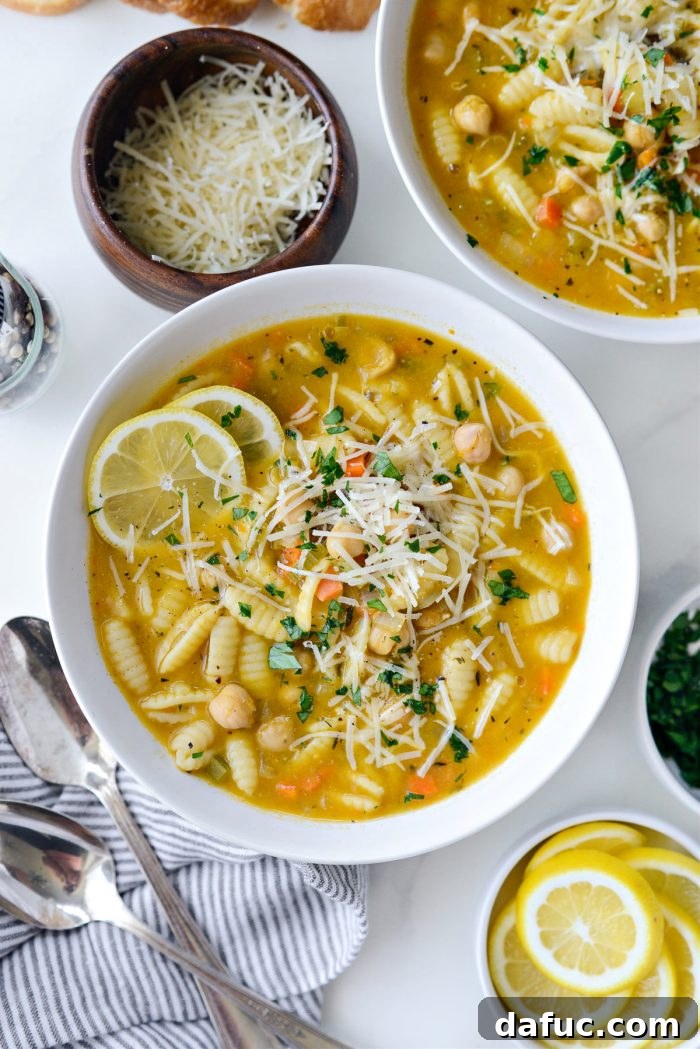 Sunshine Chickpea Bowl 16 Generously topped Lemon Chickpea Soup served in elegant bowls, beautifully garnished with a liberal sprinkle of freshly grated Parmesan cheese and vibrant minced parsley.