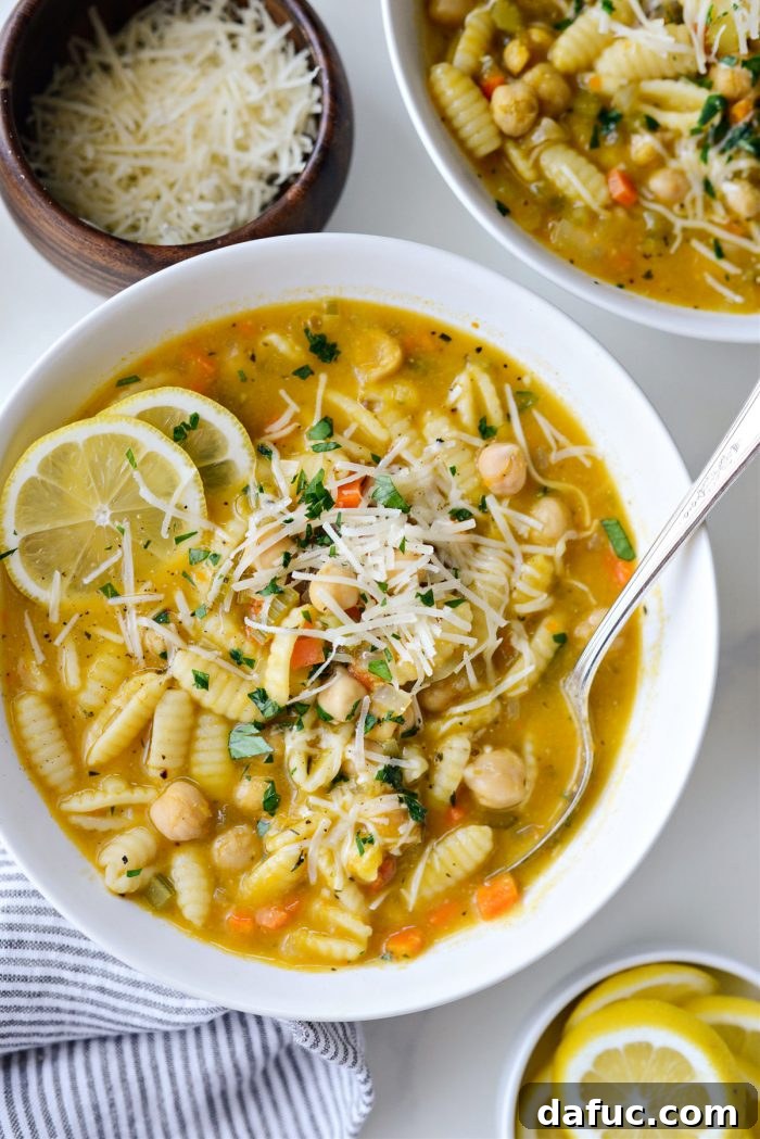 Sunshine Chickpea Bowl 18 A spoon gently dipping into a bowl of Lemon Chickpea Soup, showcasing its inviting texture and the blend of ingredients.