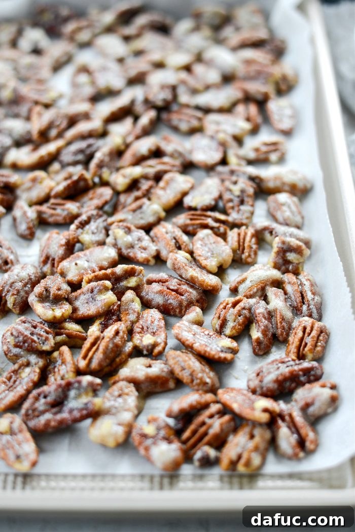 A close-up of the candied pecans on the baking sheet after 10 minutes, showing they are still somewhat wet