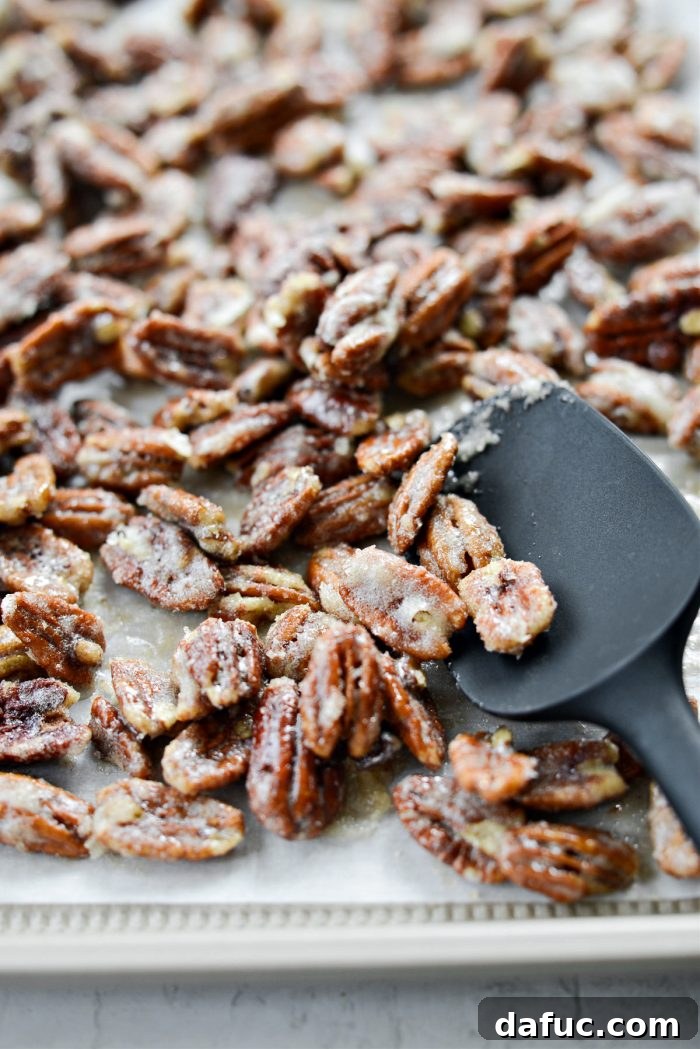 A baking sheet of candied pecans being tossed with a spatula during baking, promoting even drying