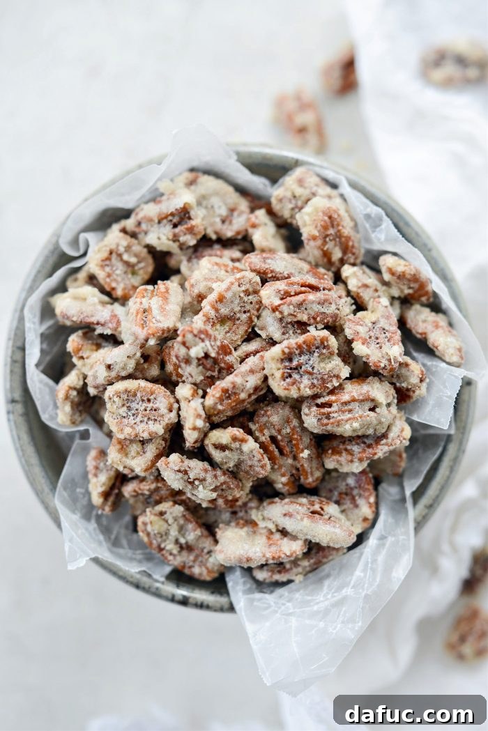 An overhead shot of a rustic wooden bowl overflowing with freshly baked candied pecans, glistening with sugar